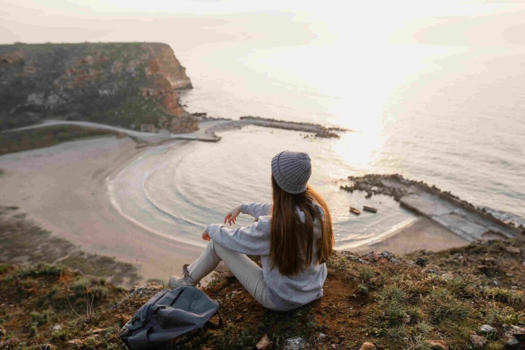 solo travelling woman sitting on a hill top gazing at the horizon